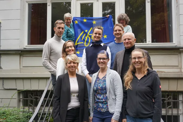 Gruppenfoto mit EU-blauer Flagge mit der Aufschrift "Life", außenherum gelbe Sterne